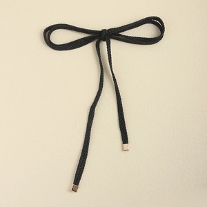 Detail of a black woven belt rope with golden metal ends tied in a delicate bow knot