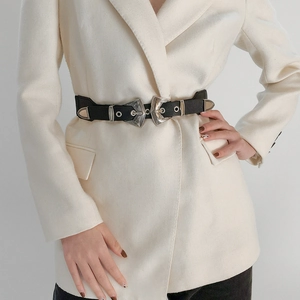 Gros plan sur les boucles métalliques gravées d'une ceinture en cuir noir sur un blazer