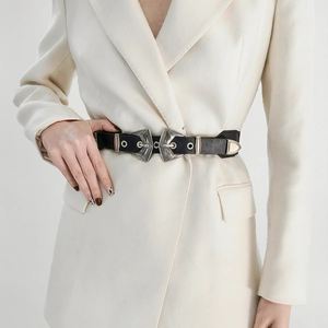 Détail des doubles boucles argentées gravées sur une ceinture en cuir noir sur un blazer crème