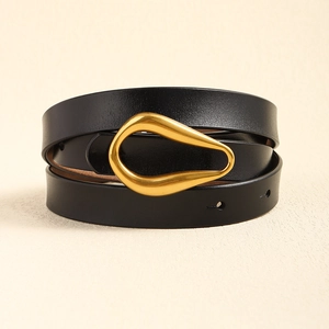 Détail d'une ceinture en cuir noir avec une boucle dorée mate de forme artistique