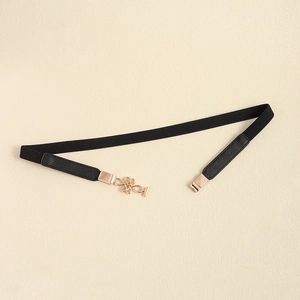 Detail of elegant gold knot buckle on slim elastic black belt with leather finish