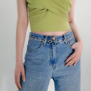 Ceinture chaîne à fleurs argentées pour femmes sur jean bleu et haut vert
