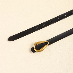 Gros plan d'une fine ceinture en cuir noir avec une boucle dorée en forme de goutte d'eau