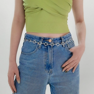 Détail d'une chaîne de taille en métal argenté avec fleurs sur un jean bleu