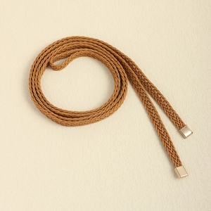 Detail of camel braided waist belt with shiny gold metal tips on textured beige backdrop