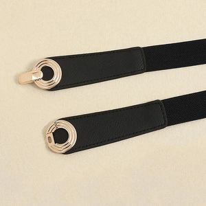 Detail of black elastic belt featuring a golden circular buckle on beige texture