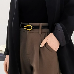 Détail d'une ceinture fine en cuir noir avec boucle dorée sur un pantalon marron