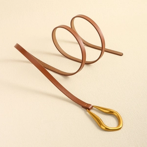 Détail d'une ceinture fine en cuir marron avec boucle dorée artistique en forme de goutte