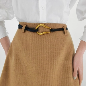 Détail d'une fine ceinture en cuir noir avec boucle goutte d'or sur une jupe