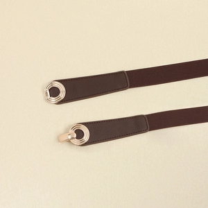 Detailed macro view of an elastic dark brown waist belt with a golden interlocking metal buckle