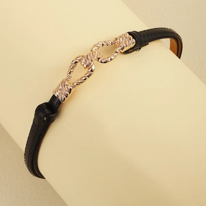 Close-up of slim black leather belt featuring an interlocking gold twist buckle detail