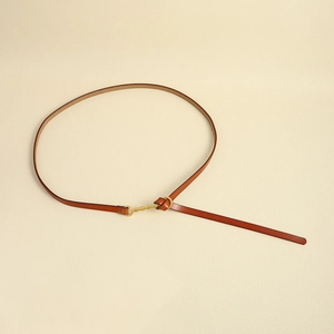 Dettaglio di una sottile cintura in pelle marrone con fibbia ad anello dorata ritorta