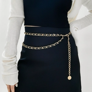 Détail de ceinture chaîne en métal doré tressé avec lanière en cuir noir et pendentif