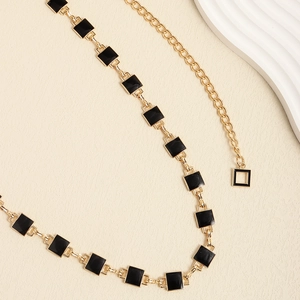Detail view of gold chain belt featuring black enamel square links and adjustable clasp