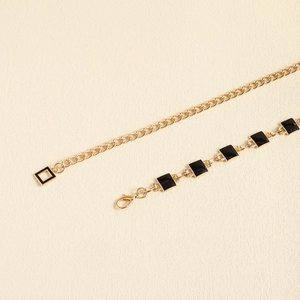 Close-up of gold metal waist chain with black enamel square links and lobster clasp