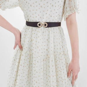 Detail of a slim black leather belt with golden double ring buckle on floral dress