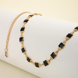 Detail of gold metal waist chain with black square enamel blocks on a white display