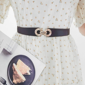 Detail of slim dark leather belt with golden double ring buckle on floral dress