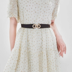 Detail of slim black elastic waist belt with gold double-ring buckle on floral dress
