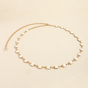 Detail of gold metal waist chain featuring white square enamel beads on a textured surface