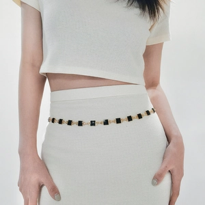 Detail of gold metal waist chain with black square enamel charms on white dress