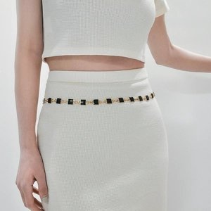 Close-up of a gold metal waist chain with square black enamel blocks on a knit dress