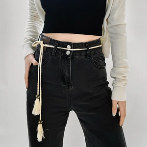 Close-up of beige woven rope belt with tassels styled on high-waist black denim jeans