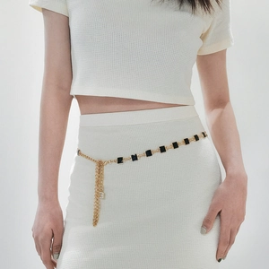 Detail of gold chain belt with black square charms and tassel on white dress