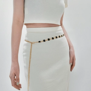 Detailed close-up of a gold thin waist chain with black square charms on white dress