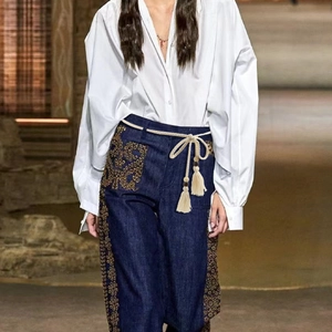 Detail of bohemian tassel rope belt on dark blue jeans with ethnic gold embroidery