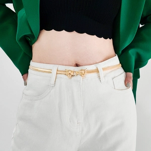 Detailed close-up of golden metal snake chain belt featuring a luxury leopard buckle on white pants