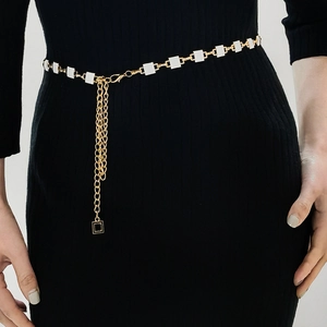 Detailed close-up of golden waist chain with white square enamel tiles on black dress