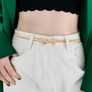 Detailed close-up of golden leopard head buckle on elastic metal belt with green blazer