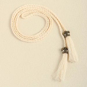 Detail of woven beige cotton tassel belt with vintage bronze fleur-de-lis metal charms