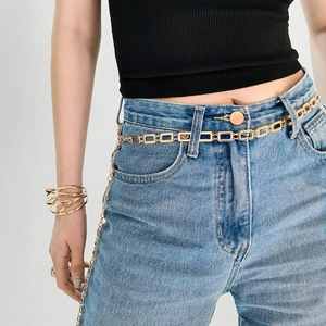 Détail d'une chaîne de taille dorée à maillons rectangulaires sur un jean femme