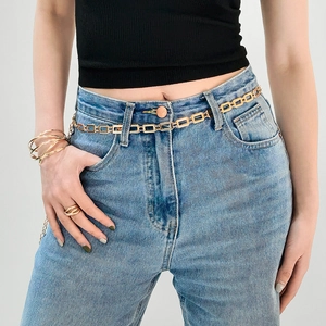 Détail d'une chaîne de corps dorée à maillons géométriques sur un jean en denim bleu