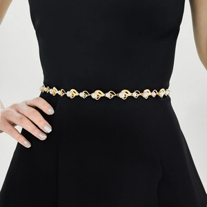 Détail d'une ceinture chaîne dorée avec perles blanches sur une robe noire ajustée