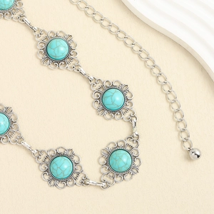 Détail de pierres turquoise serties dans une ceinture chaîne en métal argenté fleuri