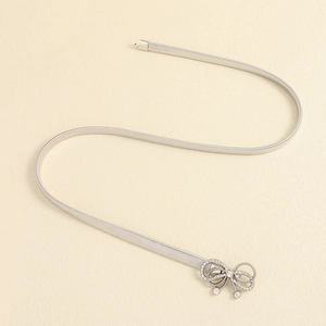 Macro detail of silver elastic metal belt featuring a bow buckle with rhinestones