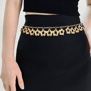 Detail of golden metal waist chain with hollow flower charms on a black dress