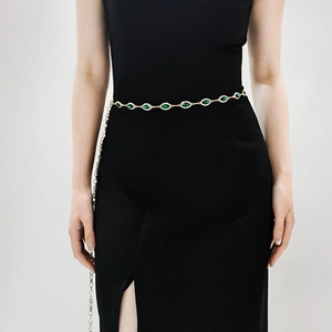 Dettaglio di un'elegante cintura a catena dorata con pietre verdi marquise su abito nero