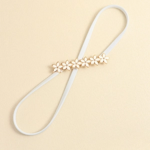 Close-up of white elastic waist belt with gold-trimmed white flower buckle detail
