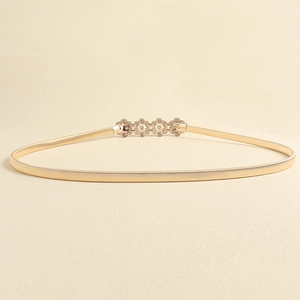 Detailed close-up of golden elastic metal waist belt with rhinestone flower buckle