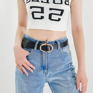 Detail of a minimalist black leather belt with a golden twisted oval alloy buckle on jeans