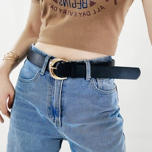 Detail of black leather belt with golden crescent buckle worn on denim jeans