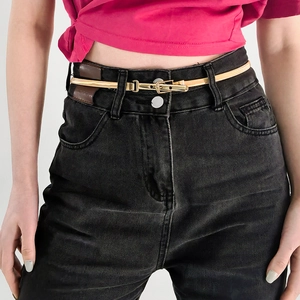 Detail of adjustable slim gold metal belt worn on dark jeans with minimalist buckle