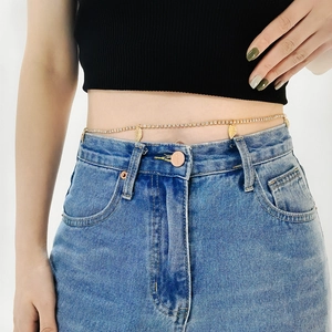 Detail shot of golden rhinestone body chain featuring leaf pendants on casual blue jeans