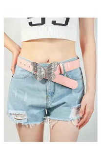 Détail d'une ceinture en cuir PU rose avec grande boucle papillon argentée sur un jean