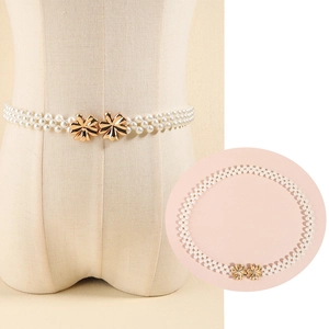 Detail of three-row pearl waist chain with gold flower buckle on beige dress