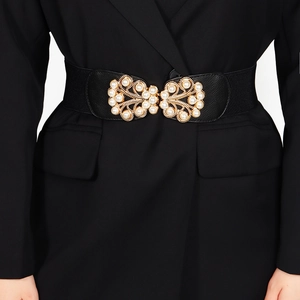 Close-up of elegant gold leaf buckle with pearls on black elastic belt for women